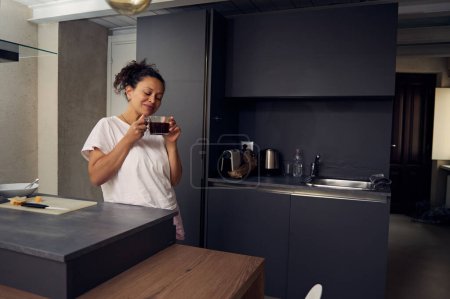 Young woman smiling while drinking coffee in the home kitchen. Start your day with energizing freshly brewed coffee