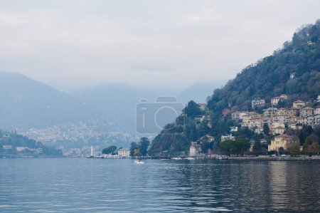 Beautiful view of Lake Como with hillside homes and misty mountains in the background. Tranquil waters and picturesque landscapes create a serene atmosphere.