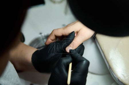 Close-up of a professional manicure being performed in a beauty salon. A technician in gloves is carefully grooming a client's nails.
