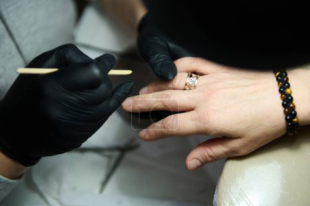 Close-up of a manicurist wearing black gloves working on a client's nails in a beauty salon. Enhancing nail beauty and care.