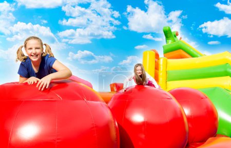 Foto de Happy little girls having lots of fun while jumping from ball to ball on an inflate castle on a sunny day outside. - Imagen libre de derechos