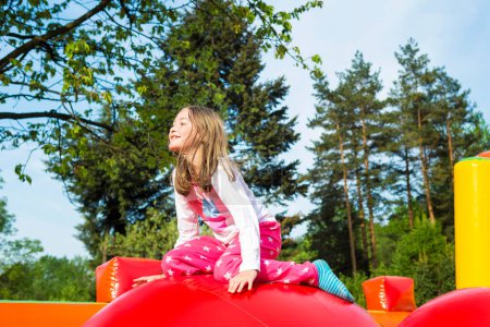 Foto de Happy smiling little girl having lots of fun on a inflate castle while jumping on big balls outdoors. - Imagen libre de derechos