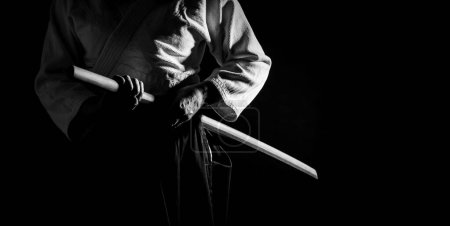 A person in black hakama standing in fighting pose with wooden sword bokken in black and white. Shallow depth of field. SDF. 