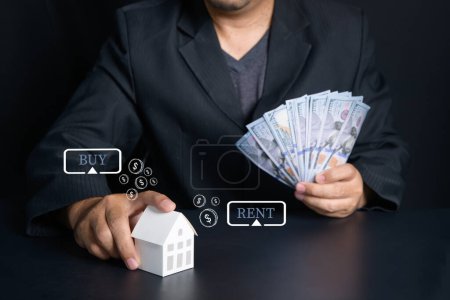 Businessman hold paper house and Dollar banknote on black background, making to rent or buy a new house concept