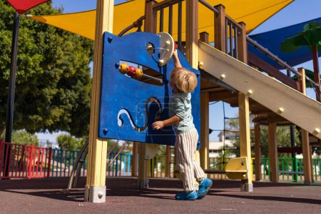 a blond boy of three years old plays on the playground
