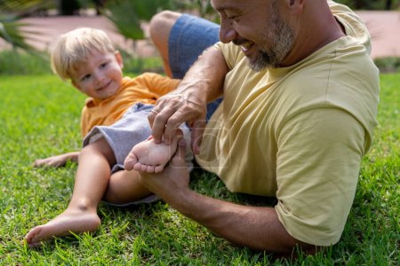 Familien- und Liebeskonzept - junger Vater kitzelt seinen kleinen Sohn im Park Nahaufnahme der Ferse eines Kindes und der Hand des Vaters, die ihn kitzelt. fröhliches Baby lacht vor dem Kitzeln