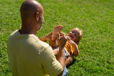 family and love concept - young father tickling his little son in park. dad tickles his son's legs on the grass. dad with little son having fun on the green lawn