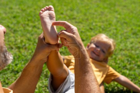 Familien- und Liebeskonzept - junger Vater kitzelt seinen kleinen Sohn im Park Nahaufnahme der Ferse eines Kindes und der Hand des Vaters, die ihn kitzelt. fröhliches Baby lacht vor dem Kitzeln