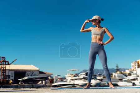People, sport and recreation concept. a fitness woman with a perfect figure stands on a mat. a girl in sports leggings, a top and a cap stands on a fitness mat.
