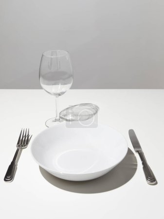 Foto de Plato blanco vacío con vaso de vino tinto vacío y tenedor con cuchillo sobre mesa blanca - Imagen libre de derechos