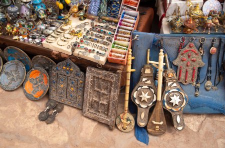Téléchargez les photos : Souvenirs marocains traditionnels - assiette, bijoux, instruments de musique et porte intérieure en bois à Ait Ben Haddou au Maroc - en image libre de droit