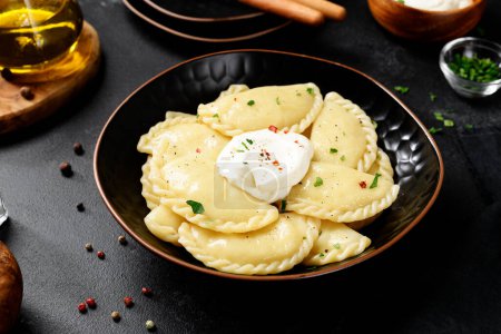 Téléchargez les photos : Boulettes bouillies avec pommes de terre servies avec de la crème sure. Cuisine traditionnelle ukrainienne ou russe. Fond noir. - en image libre de droit