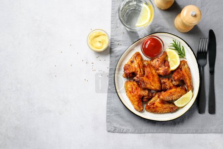Téléchargez les photos : Ailes de poulet de friteuse à air glacées à la sauce chili piquante et servies avec différentes sauces. Fond gris clair. vue de dessus - en image libre de droit