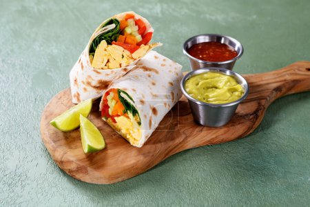 Foto de Desayuno casero burrito de huevo con verduras frescas y diferentes salsas para un desayuno vegetariano saludable. - Imagen libre de derechos