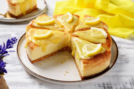Photo for Sliced Fresh baked homemade lemon cheesecake with lemon curd and lemon slices, white wooden background - Royalty Free Image