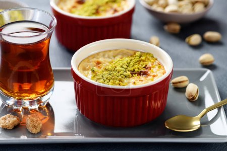 Téléchargez les photos : Pudding- traditionnel dessert au lait turc, servi avec des pistaches et une tasse de thé noir. - en image libre de droit