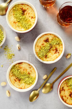 Téléchargez les photos : Pudding- traditionnel dessert au lait turc, servi avec des pistaches et une tasse de thé noir. vue de dessus - en image libre de droit