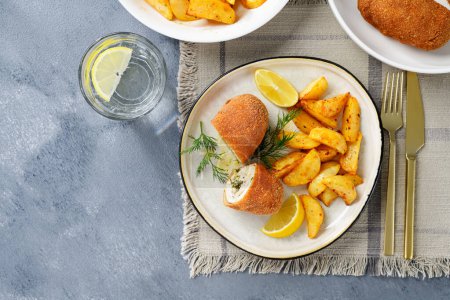 Photo for Chicken Kiev breast stuffed with butter, garlic and dill. Served with baked potato slices and fresh herbs. top view. - Royalty Free Image