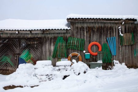 Alte Holzschuppen am See. Alles ist mit Schnee bedeckt, und die bunten Holzboote, die überall herumliegen, durchbrechen die winterliche Eintönigkeit... Trakai, Litauen.