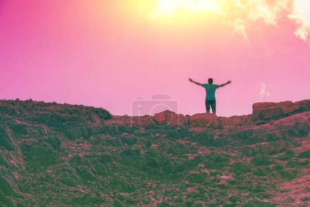 A man with hands in the air standing on the cliff in the desert