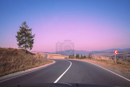 Téléchargez les photos : Vue de la route sinueuse de montagne depuis le pare-brise pendant le lever du soleil - en image libre de droit