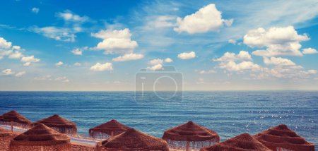 Seascape with beautiful sky and straw umbrellas on the beach on a sunny day. Horizontal banner