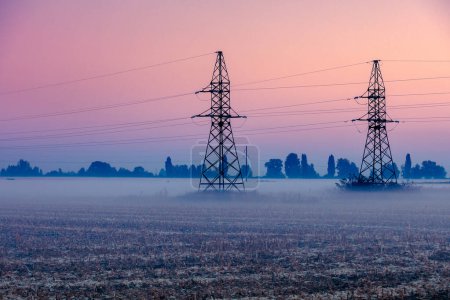 High voltage power line on a field at dawn. Foggy morning in the countryside