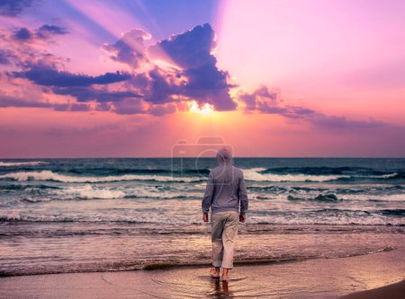 Paysage marin dans la soirée avec un beau ciel. Un homme marche pieds nus sur la plage et regarde un coucher de soleil magique