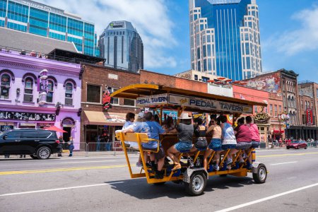 Téléchargez les photos : Nashville, Tennessee États-Unis - 9 mai 2022 : Skyline du paysage urbain du centre-ville le long de Broadway populaire avec des visiteurs profitant d'une balade sur la taverne Pedal - en image libre de droit
