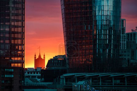 Téléchargez les photos : Tour de la Chambre des Lords à Londres vue entre les gratte-ciel. Vu au coucher du soleil. - en image libre de droit
