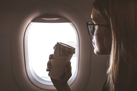 Photo for Woman passenger in the plane by the plane window. Travel and business theme. Woman drinking coffee. - Royalty Free Image