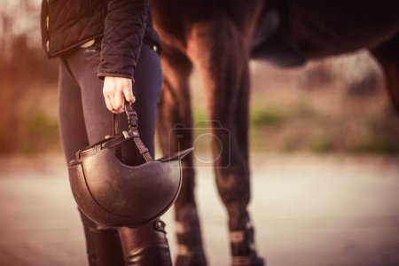 Reiterin steht neben ihrem Pferd und hält ihren Reithelm. Thema Pferdesport.