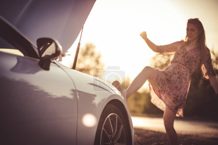 Photo for Woman kicking her broken car. Sunset. - Royalty Free Image