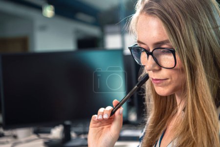 Photo for Focused office worker in glasses with a pen in her hand touching her face. Office meeting. Corporate theme. - Royalty Free Image