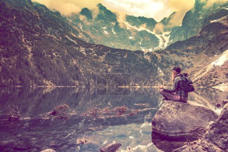 Photo for Yoga in the mountains. Searching for peace. Woman sitting on a stone in front of a mountain lake. - Royalty Free Image