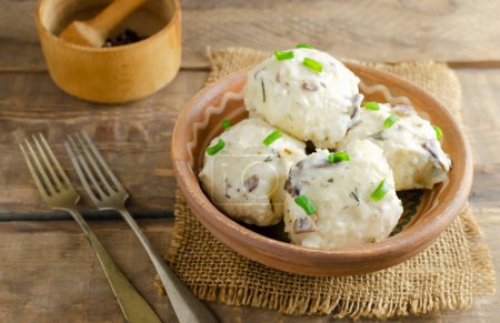 Dumplings stuffed with chicken filling with white mushroom and dill sauce on a clay plate on a wooden background. Rustic style. Concept Traditional Ukrainian cuisine. Selective focus.