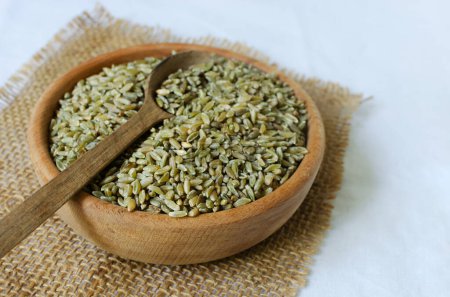 Photo for Raw freekeh or firik in a wooden bowl on burlap with a wooden spoon. Concept of healthy eating. Rustic style. Vertical orientation. Top view. Selective focus. - Royalty Free Image