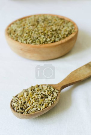 Photo for Raw freekeh or firik in wooden spoon and bowl on white background. Concept of healthy eating. Rustic style. Vertical orientation. Selective focus - Royalty Free Image