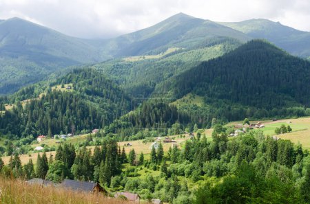 Beautiful landscape from a height. Typical Carpathian village in a valley, forest and mountains under cloudy sky. Dzembronya, Carpathians, Ukraine