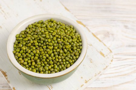 Green mung beans in a ceramic bowl on a white wooden background. Organic legumes. Vegan and vegetarian food. The concept of healthy eating. Horizontal orientation. Copy space. Selective focus.