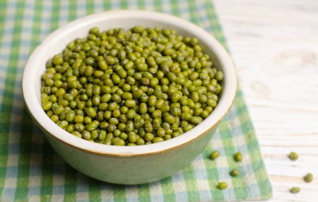 Green mung beans in a ceramic bowl on a checkered napkin. Organic legumes. Vegan and vegetarian food. The concept of healthy eating. Horizontal orientation. Copy space. Selective focus.