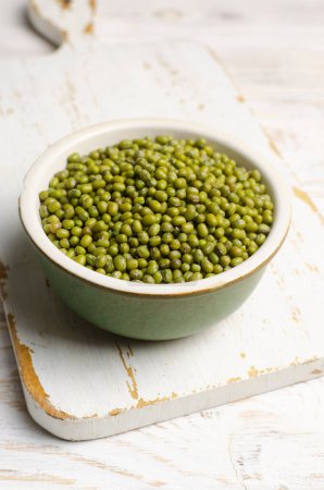 Green mung beans in a ceramic bowl on a white cutting board. Organic legumes. Vegan and vegetarian food. The concept of healthy eating. Vertical orientation. Selective focus.