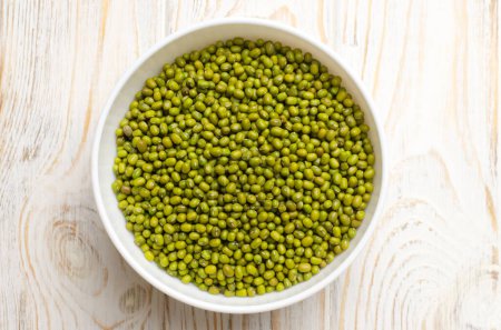 Green mung beans in a ceramic bowl on a white wooden background. Organic legumes. The concept of healthy eating. Horizontal orientation. Top view. Selective focus.