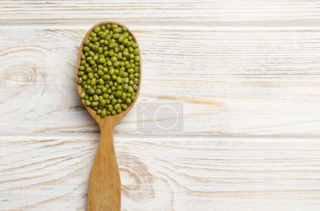 Green mung beans in a large spoon on a white wooden background. Organic legumes. Vegan and vegetarian food. The concept of healthy eating. Horizontal orientation. Copy space. Top view.