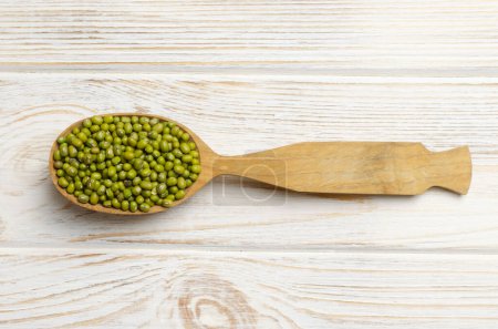 Green mung beans in a large spoon on a white wooden background. Organic legumes. Vegan and vegetarian food. The concept of healthy eating. Horizontal orientation. Top view.