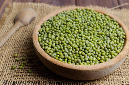 Green mung beans in a bowl on burlap on a wooden table. Organic legumes. Vegan and vegetarian food. Rustic style. The concept of healthy eating. Horizontal orientation. Selective focus.