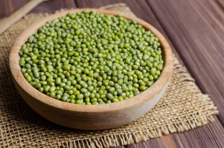 Green mung beans in a bowl on burlap on a wooden table. Organic legumes. Vegan and vegetarian food. Rustic style. The concept of healthy eating. Horizontal orientation. Copy space. Selective focus.
