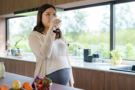 Téléchargez les photos : Charmante femme enceinte asiatique buvant du lait dans du verre. Femme attrayante besoin de protéines et de calcium pour son bébé et il la rend saine et forte. - en image libre de droit