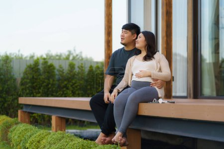 Téléchargez les photos : Asian pregnant woman with her husband talking together in terrace at home for relax and breath of fresh air. - en image libre de droit