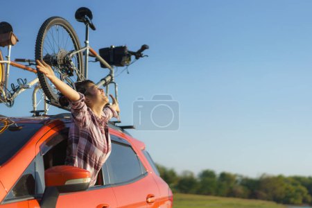 Téléchargez les photos : Asian woman pops out of car window to breathe fresh air during camping trip - en image libre de droit